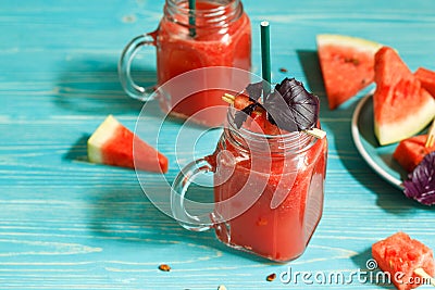 Two glass mugs with watermelon smoothie decorated with red Basil leaves. Watermelon slices on a blue wooden background. and Stock Photo