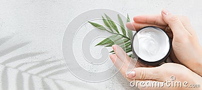 Flatlay. Woman putting nutritious cream on her hands on white background among jar of cosmetic cream, leaf palm branch Stock Photo