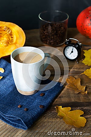 Flavored pumpkin coffee with spices in a ceramic cup on a blue napkin with orange pumpkins and dry leaves in the background.] Stock Photo