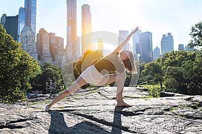 Flexible woman doing yoga pose in city park in New York at sunset time. Stock Photo