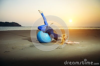 Flexible young girl with long blonde hair exercising on a yoga ball. Gymnast woman and big sports ball in the evening light Stock Photo