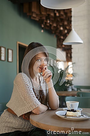 Flirtatious girl sits at table in cafe. Young woman in cafe with cup of latte or cappuccino and dessert Stock Photo