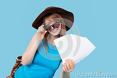 A flirtatious girl tourist in a hat with sunglasses poses and shows white empty space air ticket and flying documents to the Stock Photo