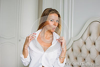 Flirting charming blonde woman with long fair hair in casual clothing sitting on the bed in bright rich interior Stock Photo