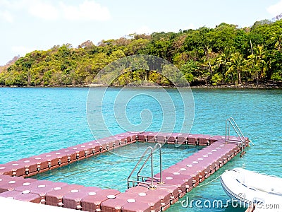 Floating swimming pool made by floating modular plastic blocks with ladder on the tropical blue sea near the speed boat and green. Stock Photo