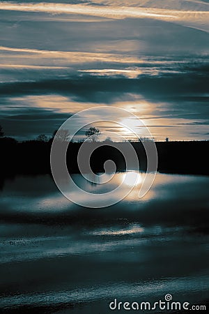 Flood in farmland field meadow at sunset with trees and sun reflected in the water. Climate change concept. Stock Photo