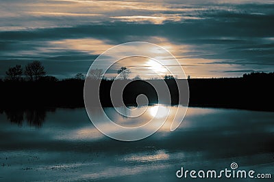 Flood in farmland field meadow at sunset with trees and sun reflected in the water. Climate change concept. Stock Photo