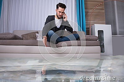 Man Sitting On Sofa Calling To Plumber Stock Photo