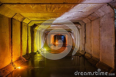 Flooded rectangular sewer tunnel with dirty urban sewage illuminated by color lights and candles Stock Photo