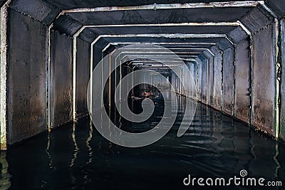 Flooded sewer tunnel is reflecting in water. Dirty urban sewage flowing throw rectangular sewer tunnel Stock Photo