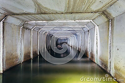 Flooded sewer tunnel is reflecting in water. Dirty urban sewage flowing throw rectangular sewer tunnel Stock Photo