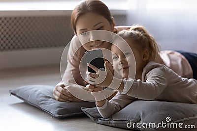 Elder sister rest on pillows with younger one use cellphone Stock Photo