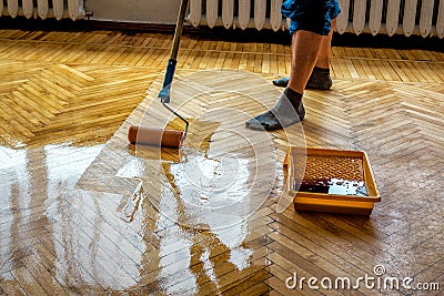 Floor renovation. Worker lacquering parquet floors using roller Stock Photo