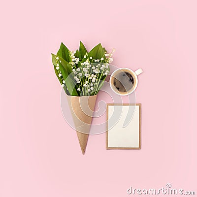 Floral springtime composition with lily of the valley, craftpaper envelope, cup of coffee, white blank card for text, mock up on Stock Photo