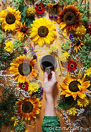Floral summer background. A mug of coffee in a woman`s hand on a wooden background with sunflowers and wildflowers Stock Photo