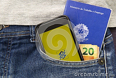 Florianopolis, Brazil. June 27, 2020: Close up of cellphone, Work brazilian card and cash in trouser pocket. Brazil Bank screen Editorial Stock Photo