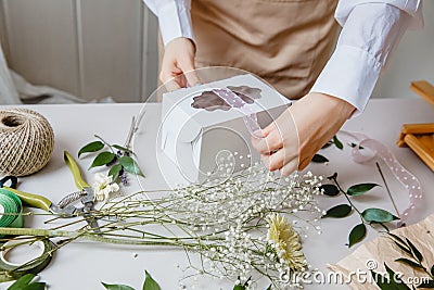 A florist decorates a gift box with flowers and a ribbon on a white desktop. Only the hands are in the frame Stock Photo
