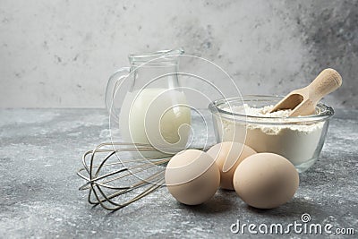 Flour, eggs, milk and whisker on marble table Stock Photo