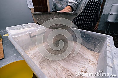 Flour sifting through a sieve for a baking. man hands, industrial Stock Photo