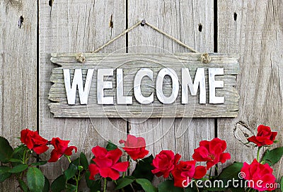 Flower border of red roses by wood welcome sign hanging on distresed wooden fence Stock Photo