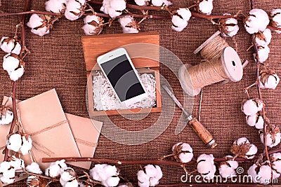 Flower design with fluffy dried cotton bolls gift boxes, white smartphone and jute rope hank over rough brown burlap Top Stock Photo