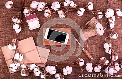 Flower design with fluffy dried cotton bolls gift boxes, white smartphone and jute rope hank over rough brown burlap Top Stock Photo
