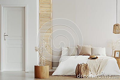 Flower on glass vase on round wooden table in beige natural bedroom, copy space on empty wall Stock Photo