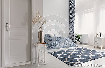 Flower in silver vase on the wooden table next to closed door to elegant new york style bedroom with patterned carpet and white fu Stock Photo