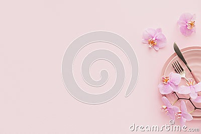 Flower and table settings overhead composition on light pink background. Pink ceramic plates, cutlery and perple orchid flowers. Stock Photo