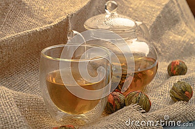 Flower tea brewed in a glass teapot, a glass of tea and balls of flower tea on a background of rough homespun fabric. Close up Stock Photo