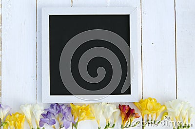 Flowers with blank black chalkboard picture frame on a light wooden background. romantic picture. Stock Photo