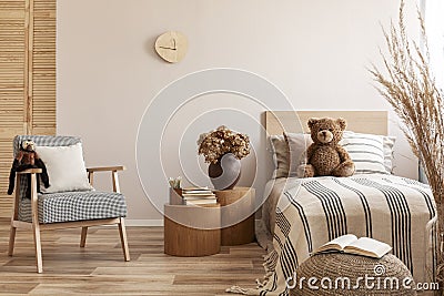 Flowers in brown vase on wooden nightstand table next to single bed with stripped bedding with teddy bear Stock Photo