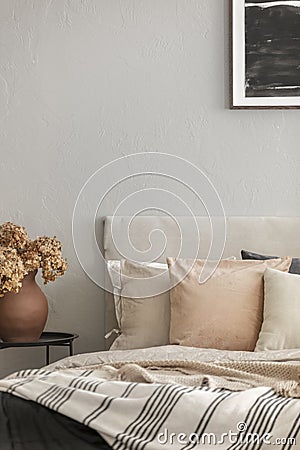 Brown flowers in pottery vase on metal nightstand next to king size bed in scandinavian bedroom interior Stock Photo