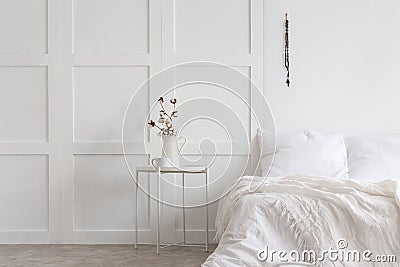 Flowers on table next to bed with pillows and sheets in white minimal bedroom interior Stock Photo