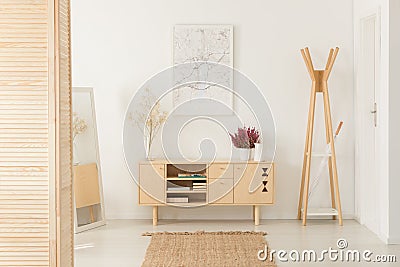 Flowers on wooden cupboard next to rack in white entrance hall interior with poster Stock Photo