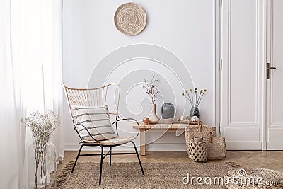 Flowers on wooden stool next to armchair in white loft interior with pouf and plate. Real photo Stock Photo