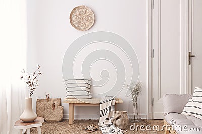 Flowers on wooden table near bench with pillow and blanket in white living room interior. Real photo Stock Photo