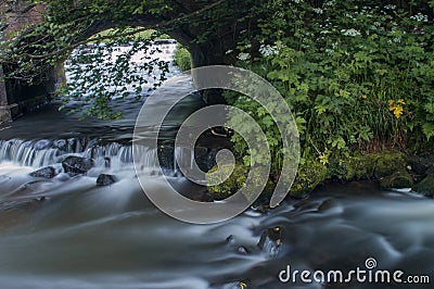 Flowing water turned milky white by a long exposure as it flows around green and brown mossy rocks. Stock Photo