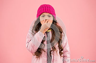 Flu season. Sneezing. Cold climate weather. Little girl sick ill pink background. Kid puffer jacket and knitted hat Stock Photo