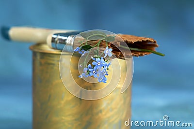 A fluted brush in golden paint with a branch of forget-me-nots in the bristles on a blue background. Selective focus Stock Photo