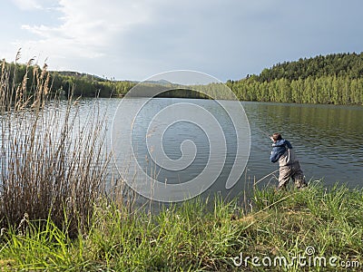 Fly Fisherman angler standing on shore of calm water of forest lake, fish pond Kunraticky rybnik with birch and spruce Editorial Stock Photo