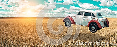 Flying car soars into the sky. Retro automobile hovers in the air above a golden wheat field on the background of blue sky. Stock Photo