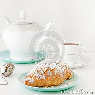 Flying food concept. Powdered sugar falling on freshly baked croissant on white breakfast table with teapot and tea. Stock Photo