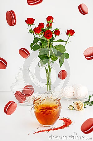 Flying food and still life. Breakfast desserts on white background with macaroons, bouquet of red roses and splashing tea Stock Photo