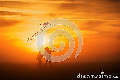 Flying a kite. Girl and boy fly a kite in the endless field. Bright sunset. Silhouettes of people against the sky Stock Photo