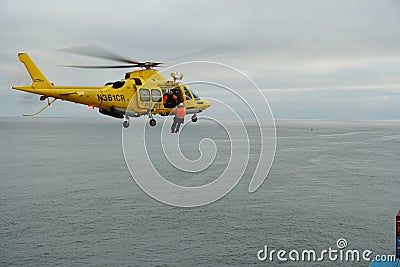 Flying yellow helicopter with hanging pilot on the rope ready for embarking merchant container vessel. Editorial Stock Photo