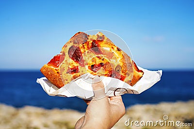 Focaccia barese slice with Mediterranean sea on background. Focaccia pugliese against blue sea and sky. Bari-style focaccia bread Stock Photo