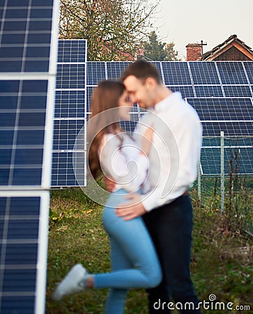 Loving couple embracing enjoying each other on background of row solar panels at plantation near the house Stock Photo