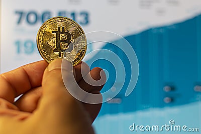 Focus on bitcoin in hand against the background of a graph of growing cryptocurrency. Concept: cryptocurrencies growth, virtual Stock Photo