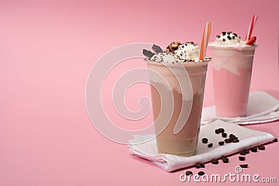 Focus of disposable cups of chocolate and strawberry milkshakes with coffee grains on napkins on pink background Stock Photo